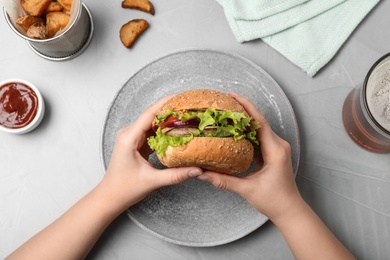 Photo of Woman holding tasty burger over plate at table, top view