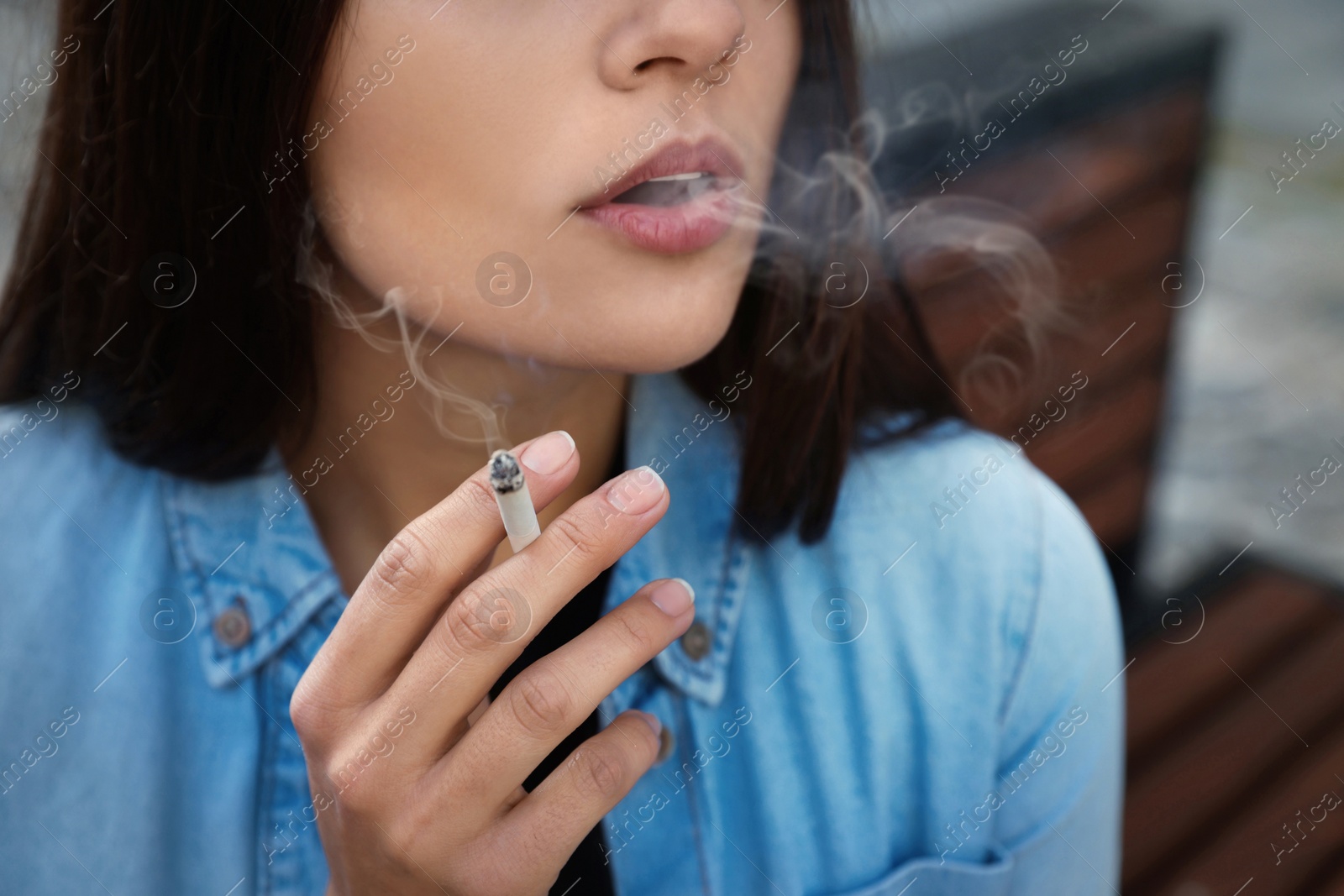 Photo of Young woman smoking cigarette outdoors, closeup view