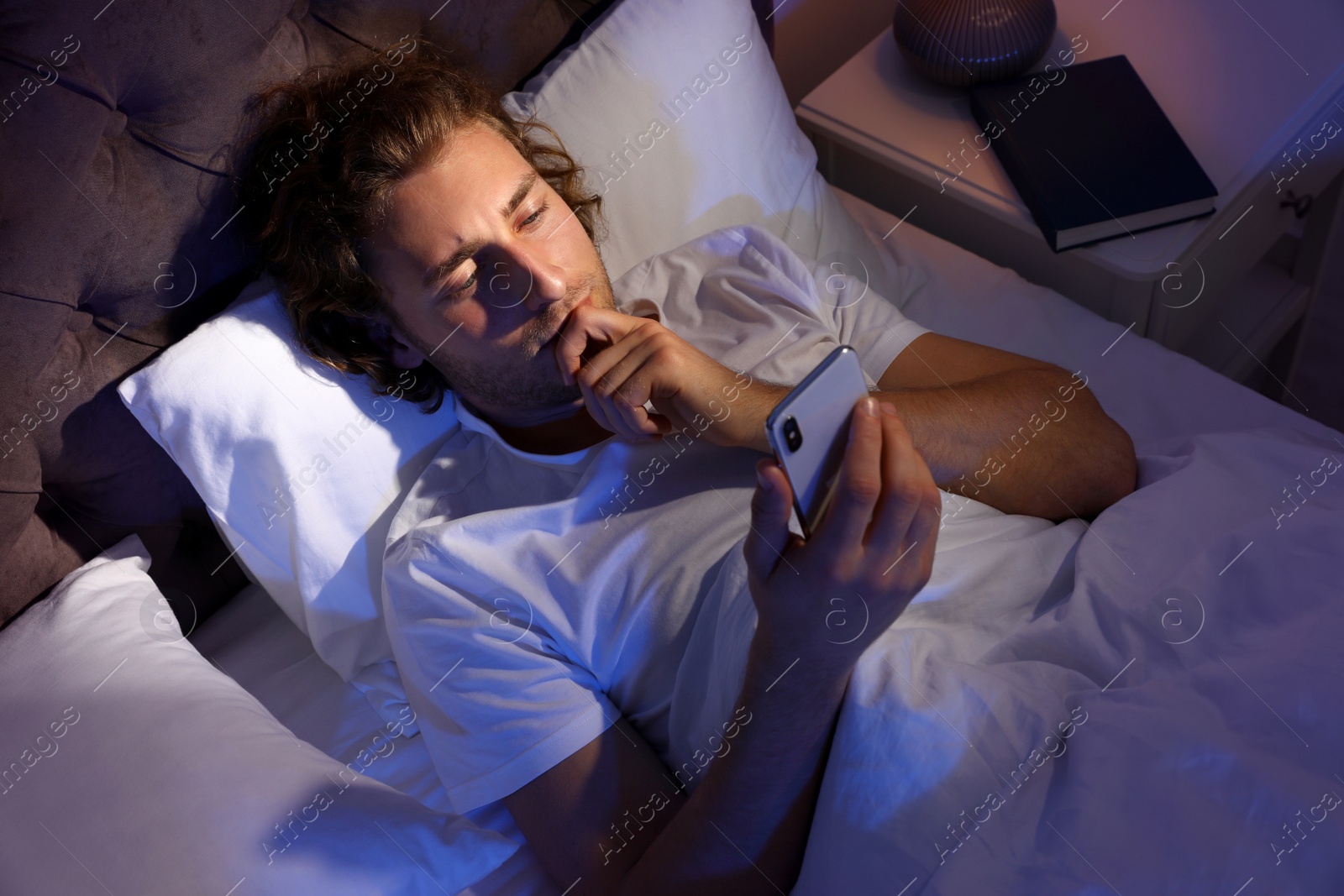 Photo of Handsome young man using smartphone in dark room at night. Bedtime