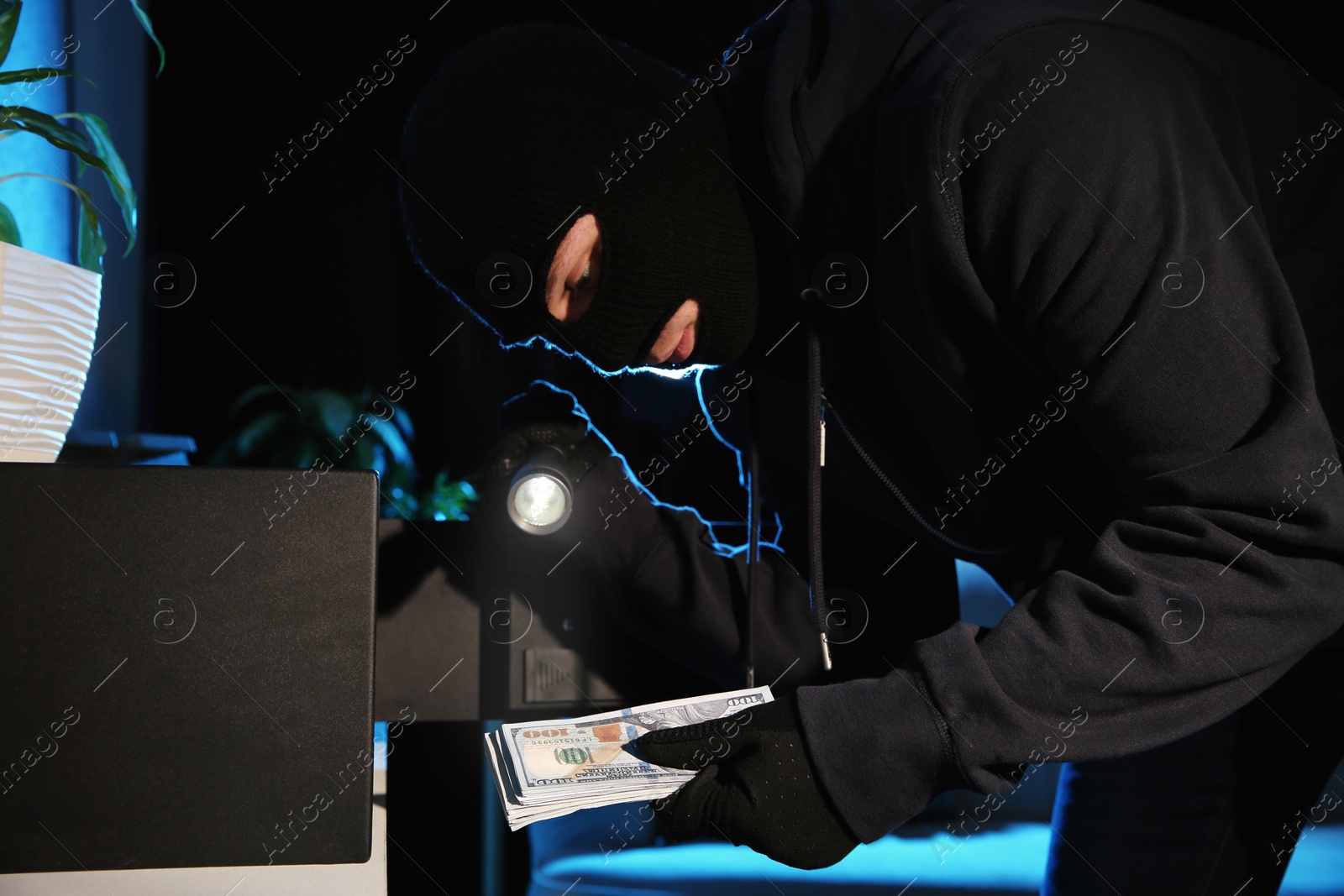 Photo of Thief taking money out of steel safe indoors at night