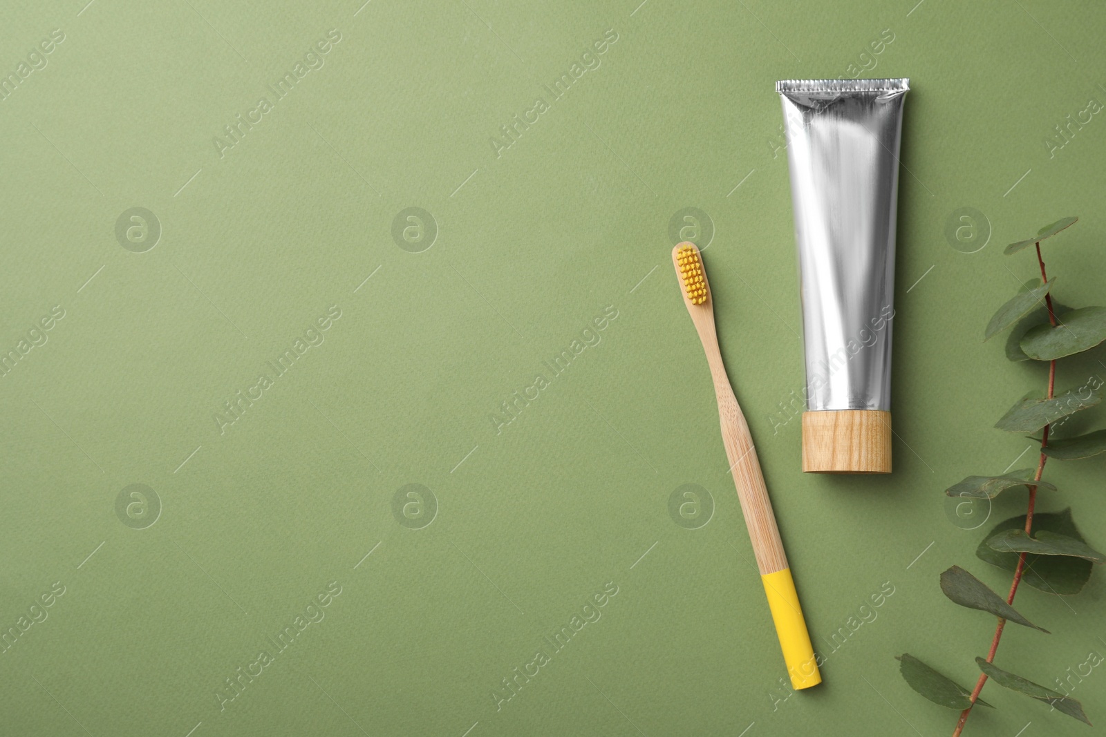 Photo of Bamboo toothbrush, tube of paste and space for text on green background, flat lay. Conscious consumption