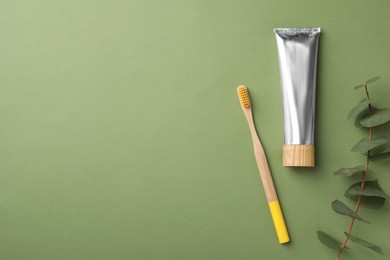 Bamboo toothbrush, tube of paste and space for text on green background, flat lay. Conscious consumption
