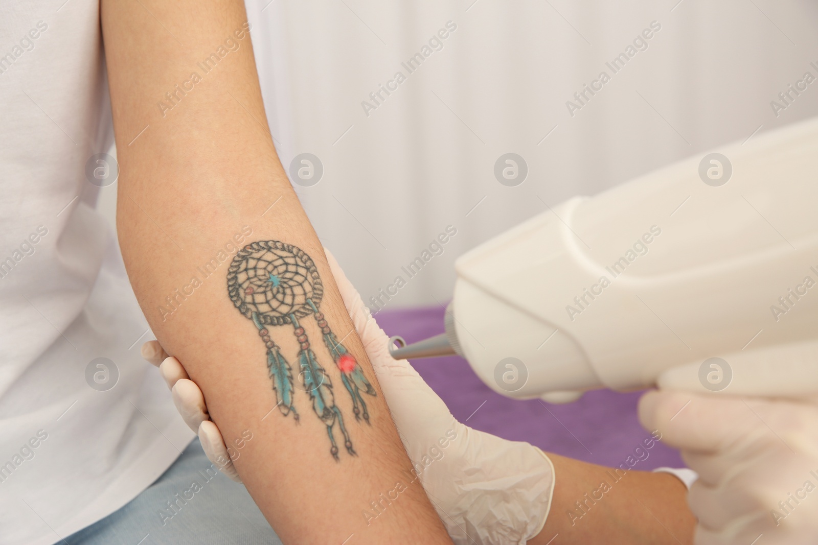 Photo of Young woman undergoing laser tattoo removal procedure in salon, closeup