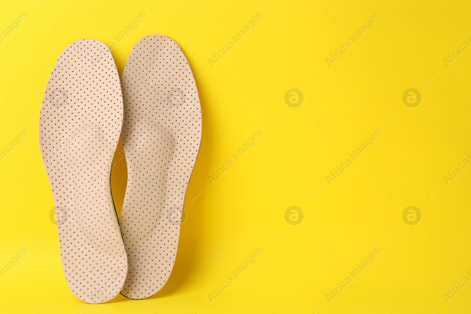Photo of Beige orthopedic insoles on yellow background, flat lay. Space for text