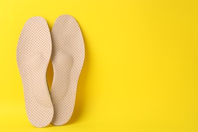 Photo of Beige orthopedic insoles on yellow background, flat lay. Space for text