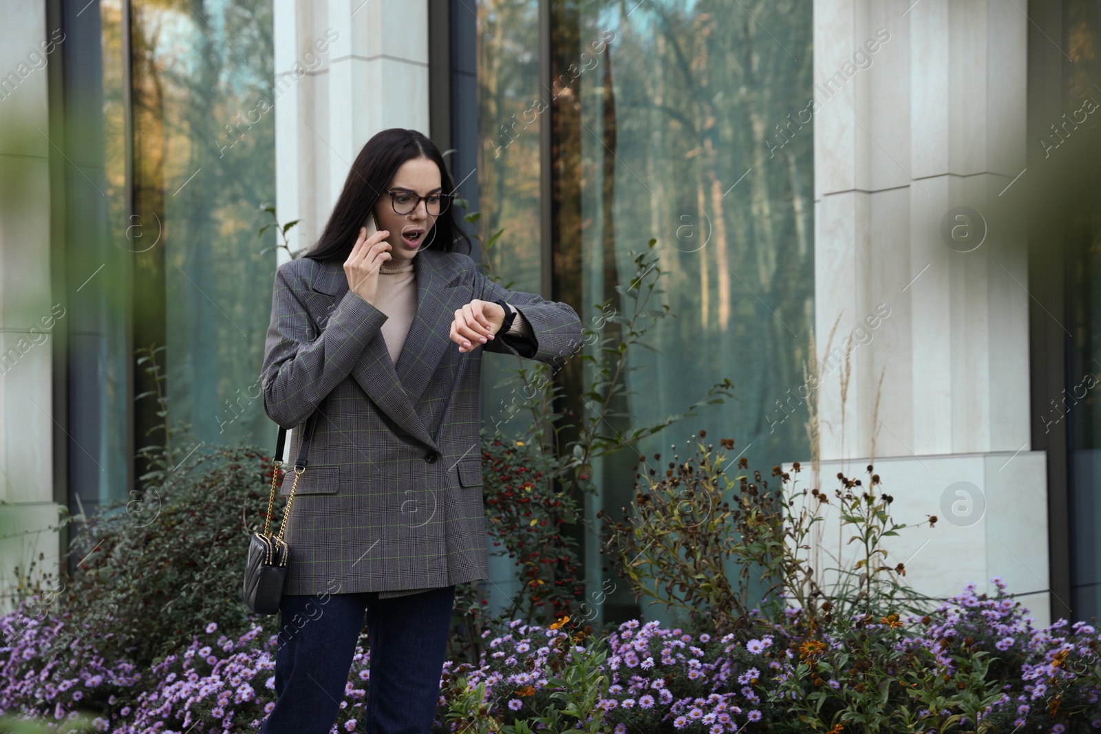 Photo of Emotional woman checking time while talking on smartphone outdoors. Being late concept