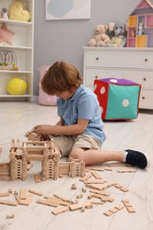 Photo of Little boy playing with wooden construction set on floor in room. Child's toy