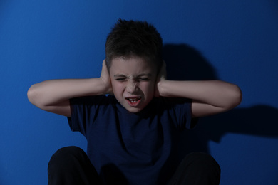 Photo of Scared little boy closing his ears near blue wall. Domestic violence concept