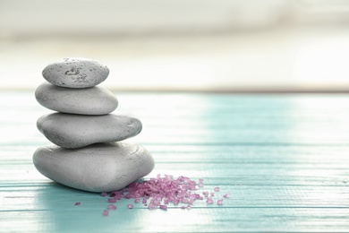 Photo of Spa stones and sea salt on table against blurred background. Space for text