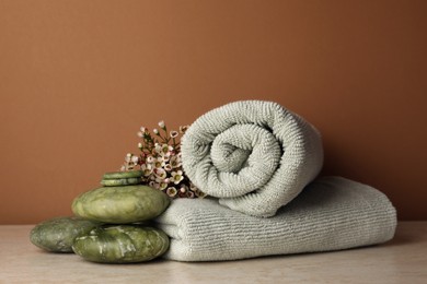 Photo of Composition with spa stones, towels and flowers on beige table against brown background. Space for text