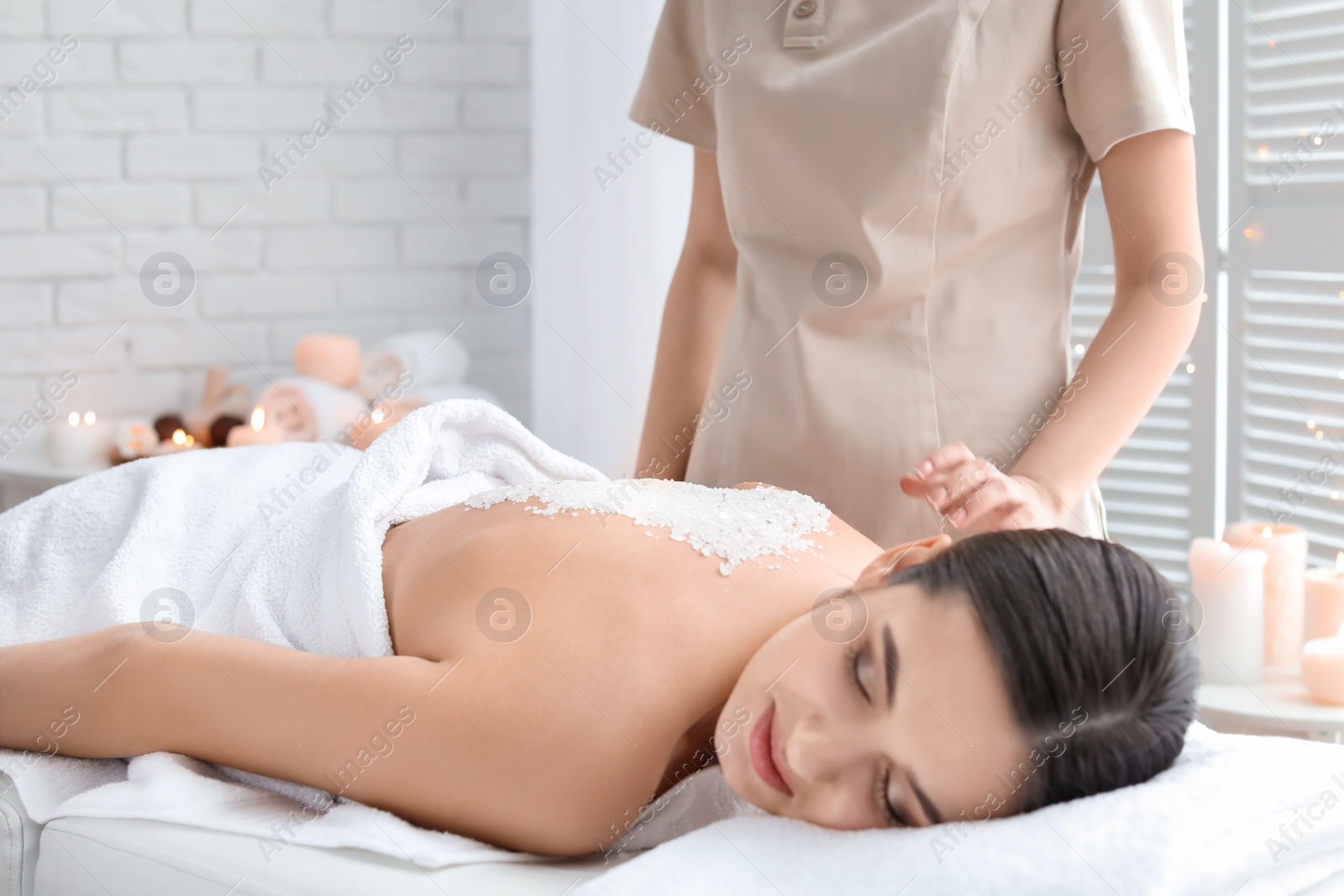 Photo of Young woman having body scrubbing procedure with sea salt in spa salon