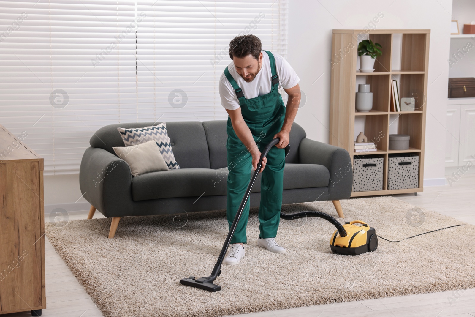 Photo of Dry cleaner's employee hoovering carpet with vacuum cleaner in room