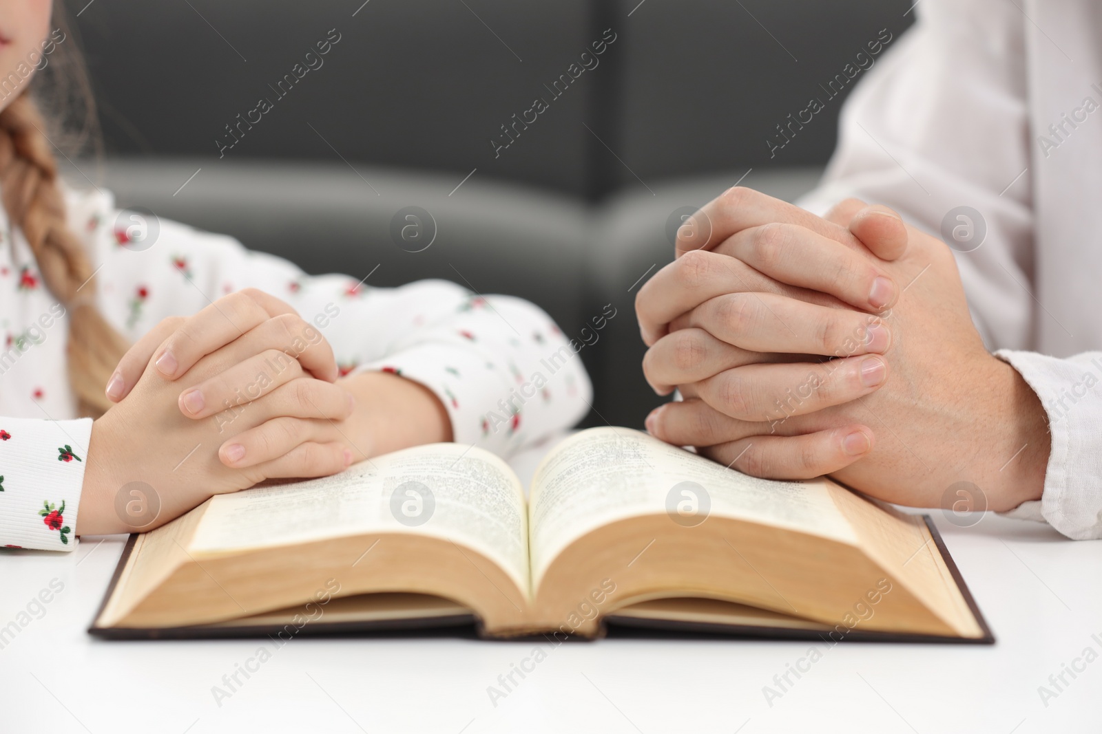 Photo of Girl and her godparent praying over Bible together at table indoors, closeup