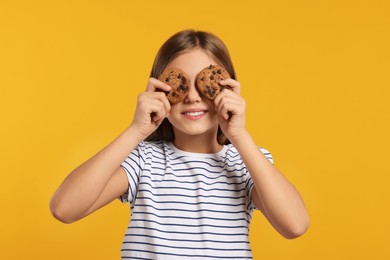 Photo of Girl covering eyes with chocolate chip cookies on orange background