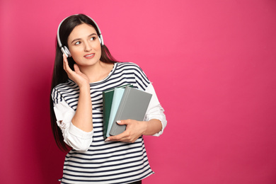 Young woman listening to audiobook on pink background. Space for text