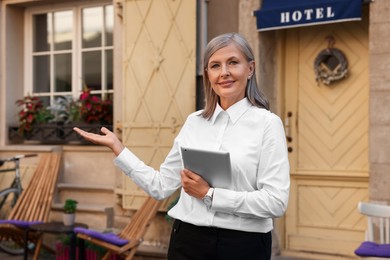 Photo of Smiling business owner with tablet inviting to come into her hotel outdoors