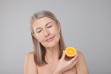 Beautiful woman with half of orange rich in vitamin C on grey background