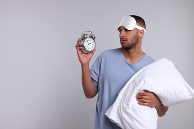Photo of Tired man with pillow, sleep mask and alarm clock on light grey background, space for text. Insomnia problem
