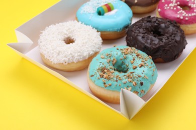 Photo of Box with tasty glazed donuts on yellow background, closeup