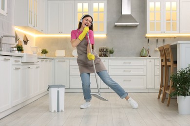 Photo of Enjoying cleaning. Happy woman with mop singing while tidying up in kitchen