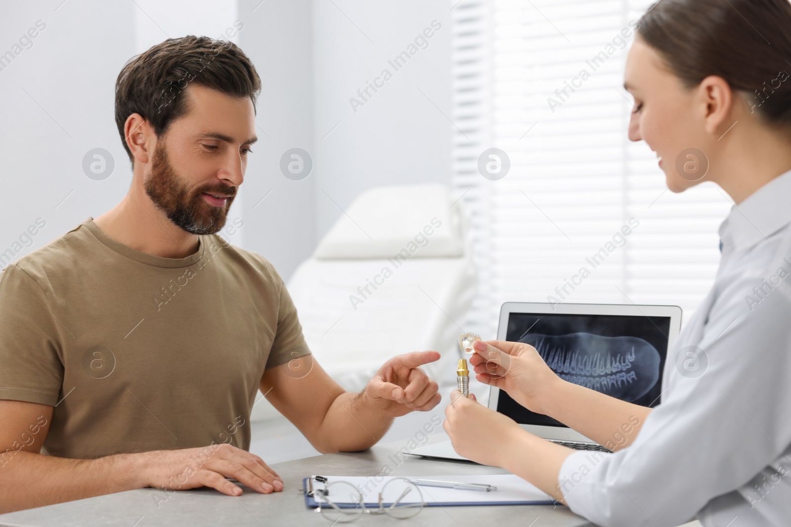 Photo of Doctor showing patient educational model of dental implant in clinic