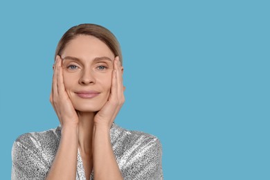 Photo of Woman massaging her face on turquoise background. Space for text