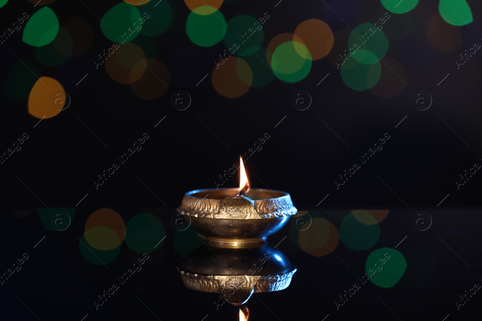 Photo of Lit diya on dark background with blurred lights, space for text. Diwali lamp