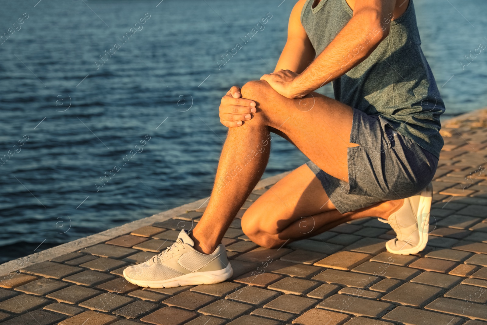 Photo of Man in sportswear having knee problems near river at sunset, closeup