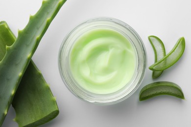 Jar of cosmetic cream and cut aloe leaves on white background, flat lay