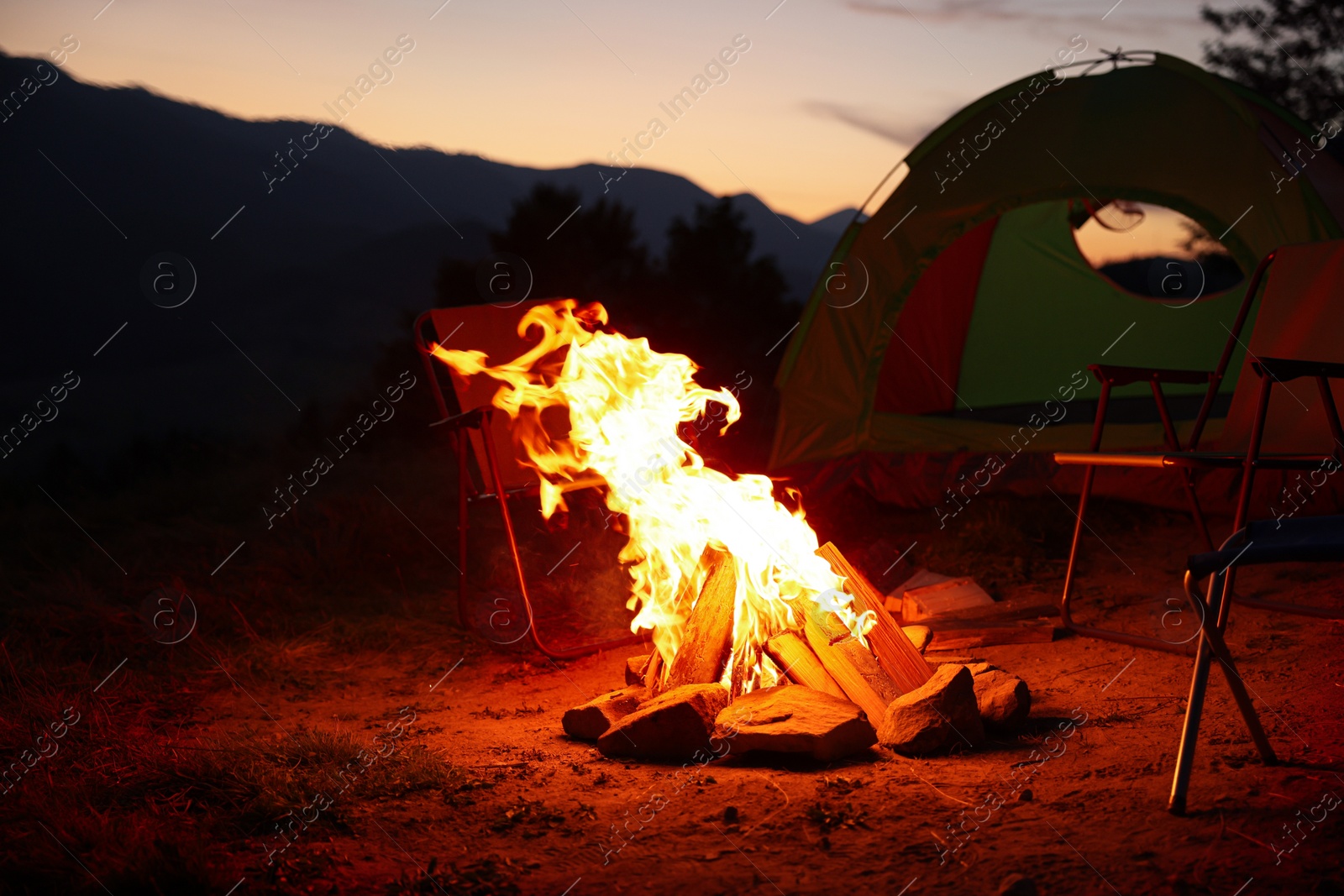 Photo of Beautiful bonfire and folding chairs near camping tent outdoors in evening