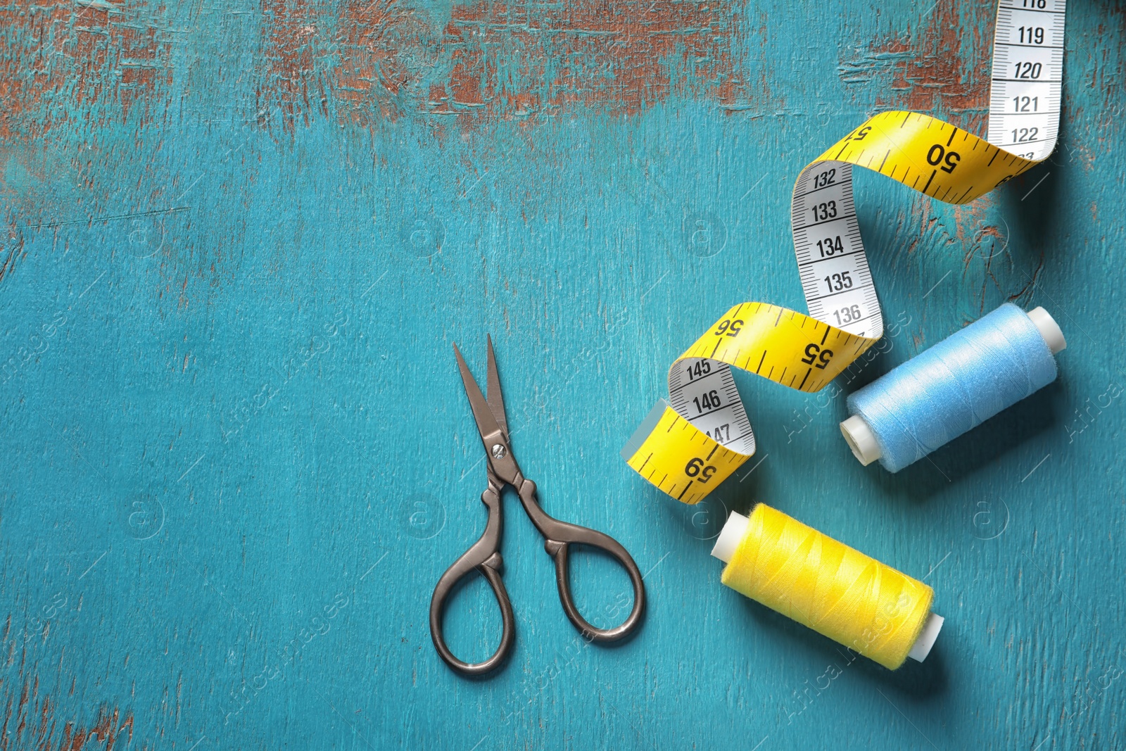 Photo of Measuring tape, scissors and threads on wooden background, top view. Tailoring equipment