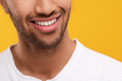 Photo of Smiling man with healthy clean teeth on orange background, closeup