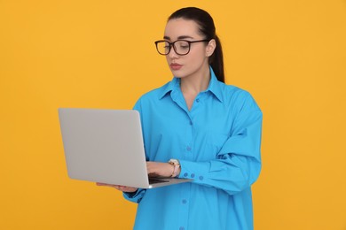 Young female intern with laptop on yellow background