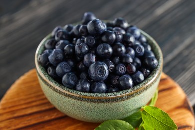 Photo of Bowl of tasty fresh bilberries on wooden table, closeup