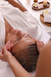 Woman receiving facial massage with rose quartz gua sha tool in beauty salon, closeup