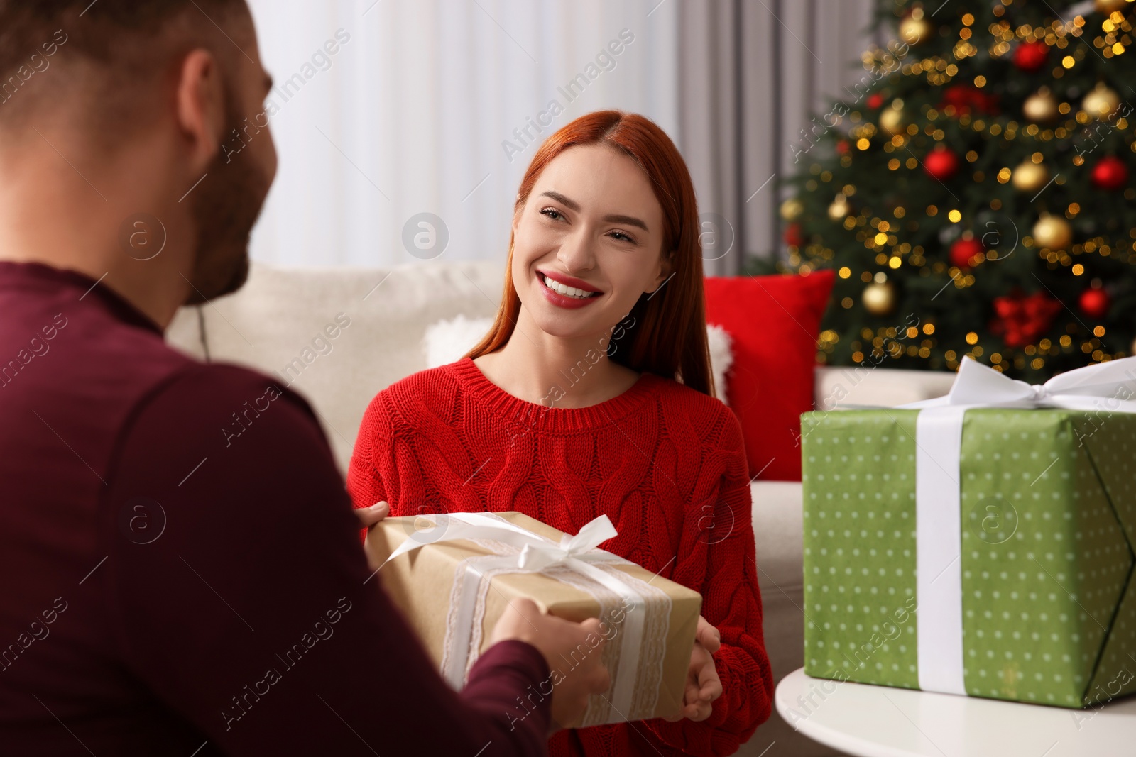 Photo of Christmas celebration. Woman and man exchanging gifts at home