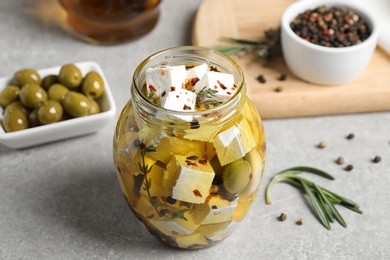 Jar with feta cheese marinated in oil on light grey table. Pickled food