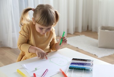 Photo of Cute little girl drawing with marker at white table indoors. Child`s art