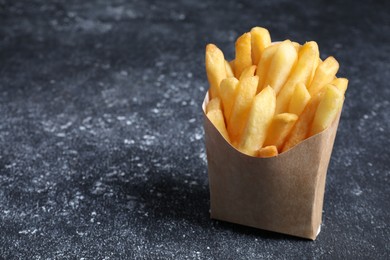 Delicious french fries in paper box on black textured table, space for text