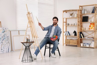 Photo of Happy man painting in studio. Using easel to hold canvas