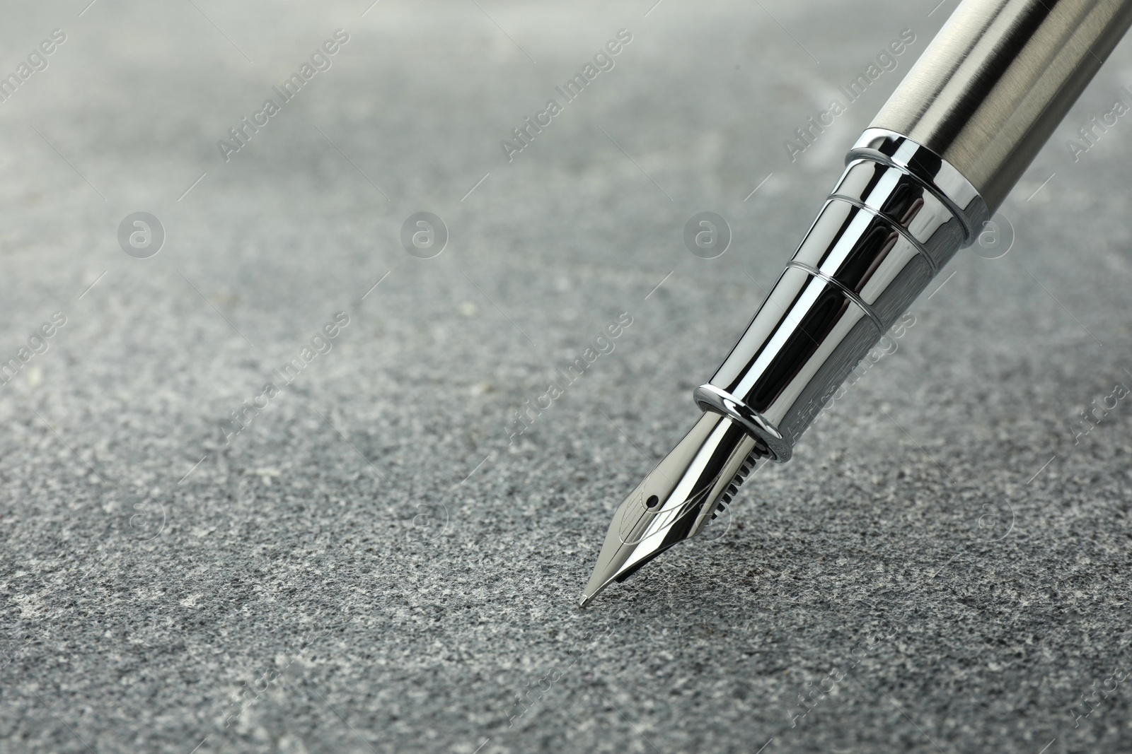 Photo of Stylish silver fountain pen on grey textured table, closeup. Space for text