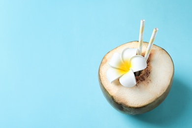 Fresh green coconut with drinking straws and flower on color background