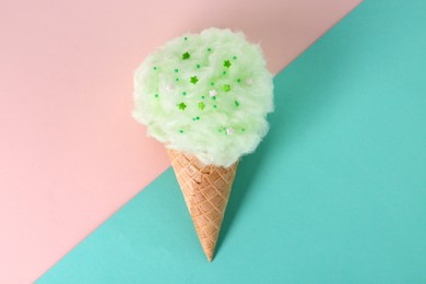 Sweet cotton candy in waffle cone on color background, top view