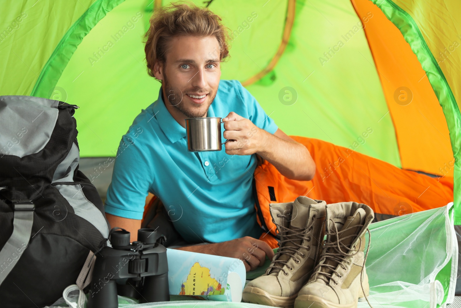 Photo of Young man in sleeping bag with mug inside of tent