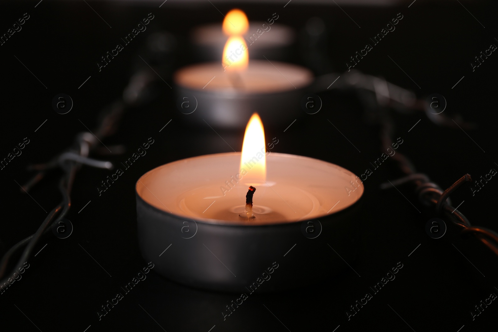 Photo of Burning candle and barbed wire on black background, closeup. Holocaust memory day