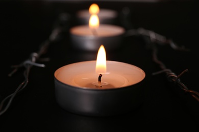 Photo of Burning candle and barbed wire on black background, closeup. Holocaust memory day