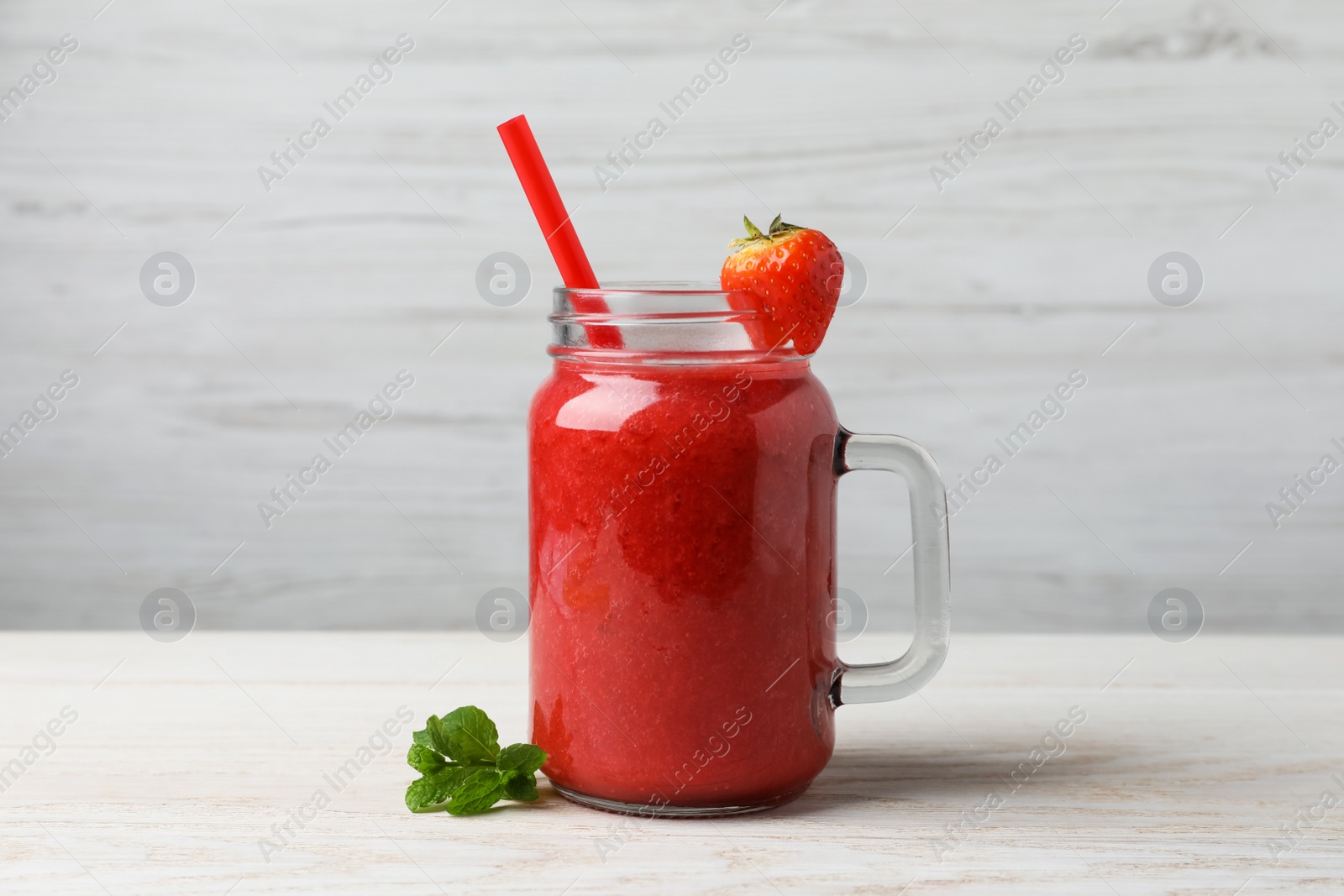Photo of Mason jar with delicious strawberry smoothie and fresh berry on white wooden table