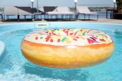 Photo of Bright inflatable doughnut ring floating in swimming pool on sunny day, outdoors