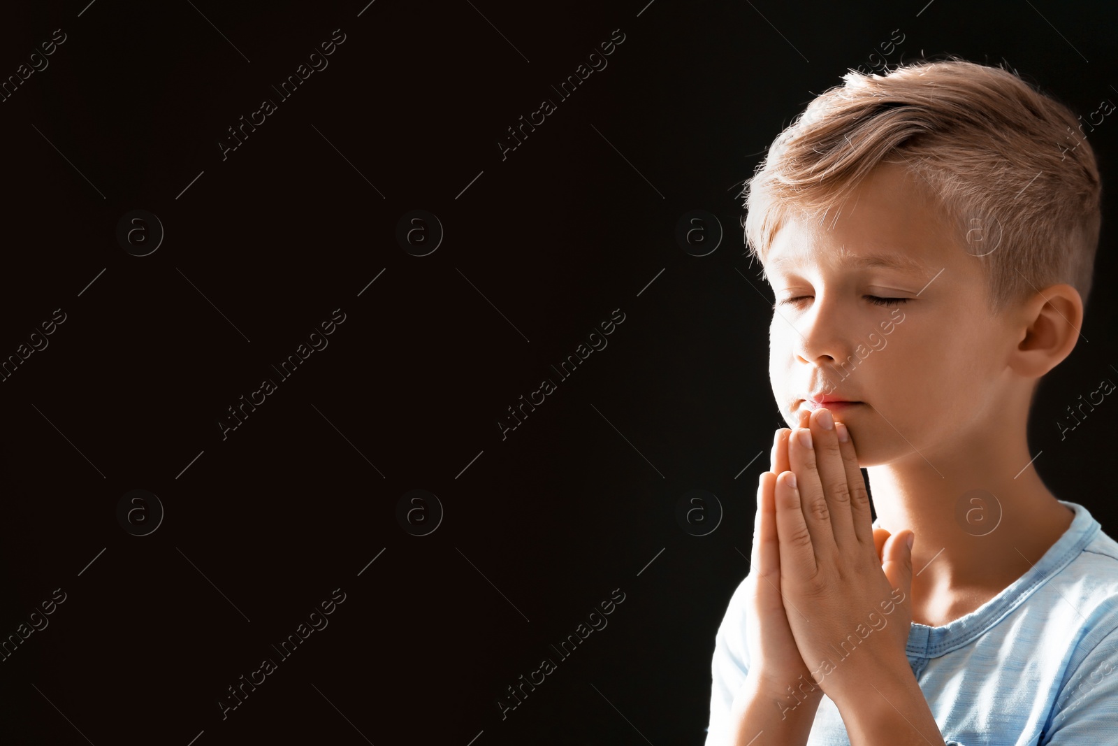 Photo of Little boy with hands clasped together for prayer on black background. Space for text