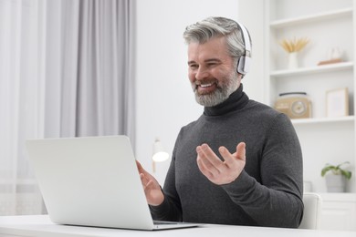 Man in headphones waving hello during video chat via laptop at home